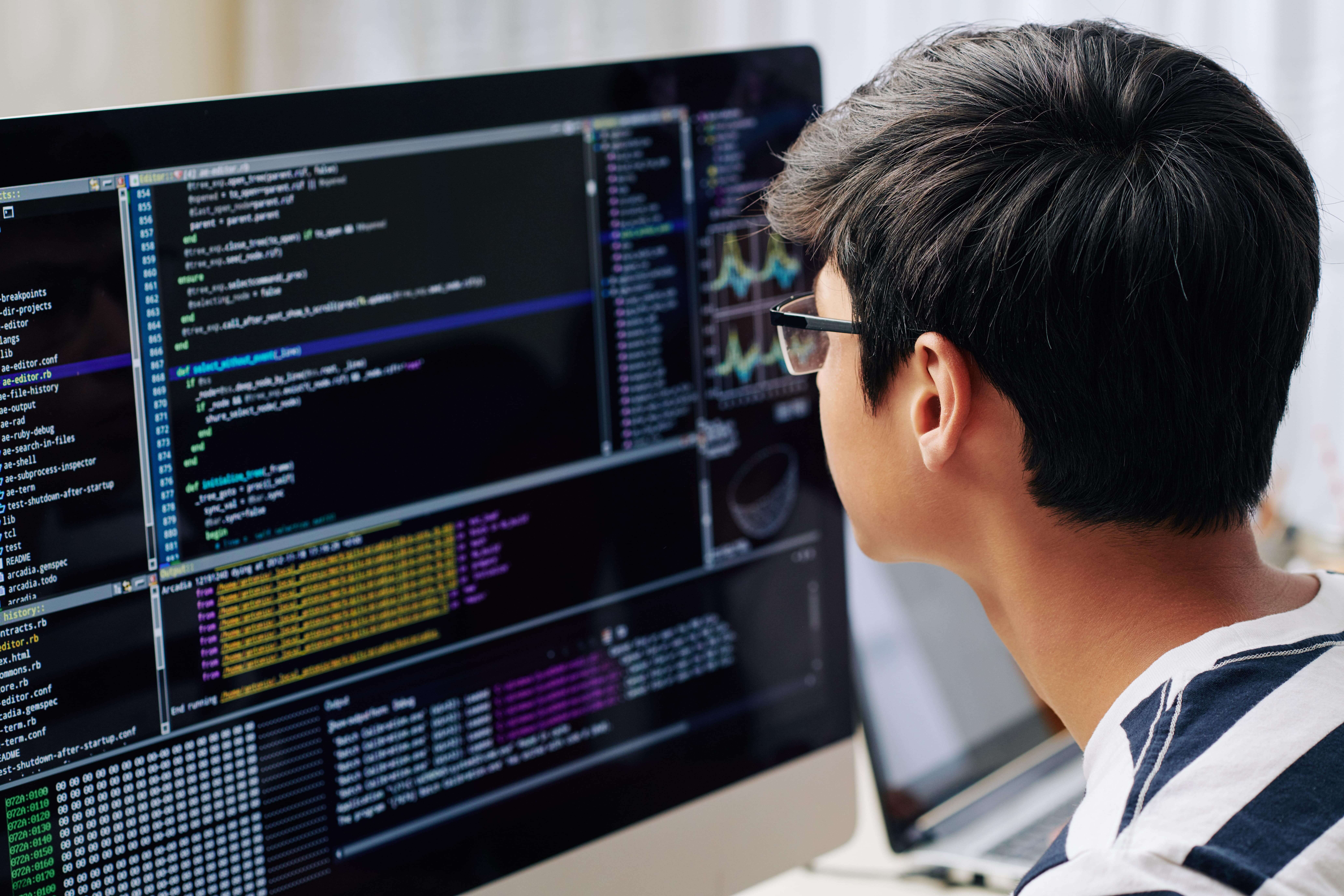 A teenage boy writing code on a desktop